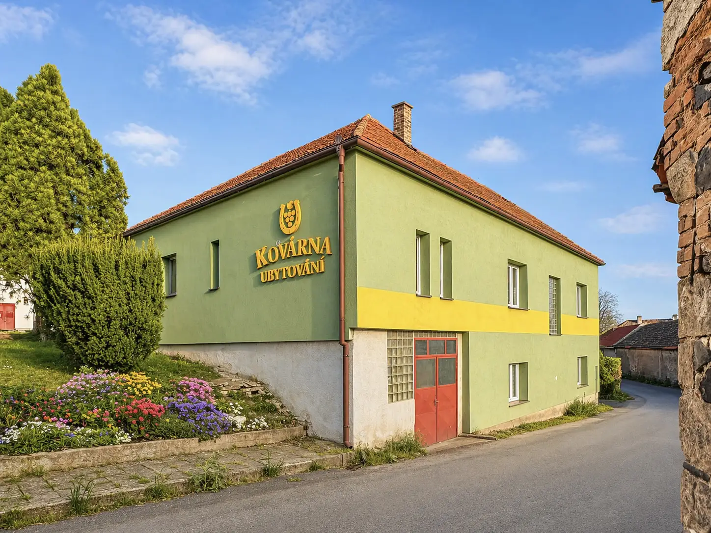 Exteriér ubytování Kovárna Klapý, zelená fasáda s nepřehlédnutelným žlutým nápisem a logem podkovy.